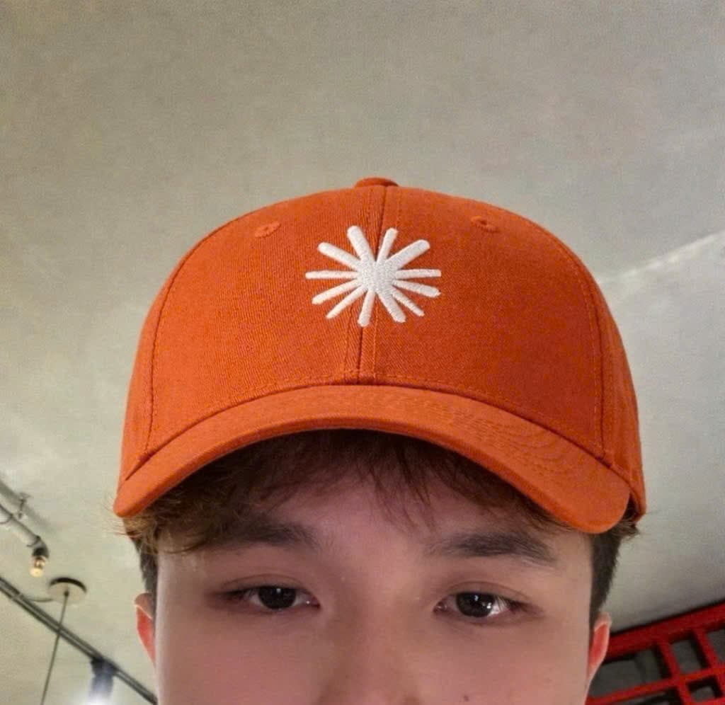 Hà in an orange cap with a white flower logo, close up